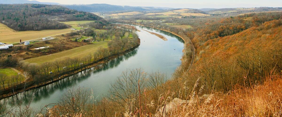 A river winding through a valley with fields and trees, surrounded by hills.
