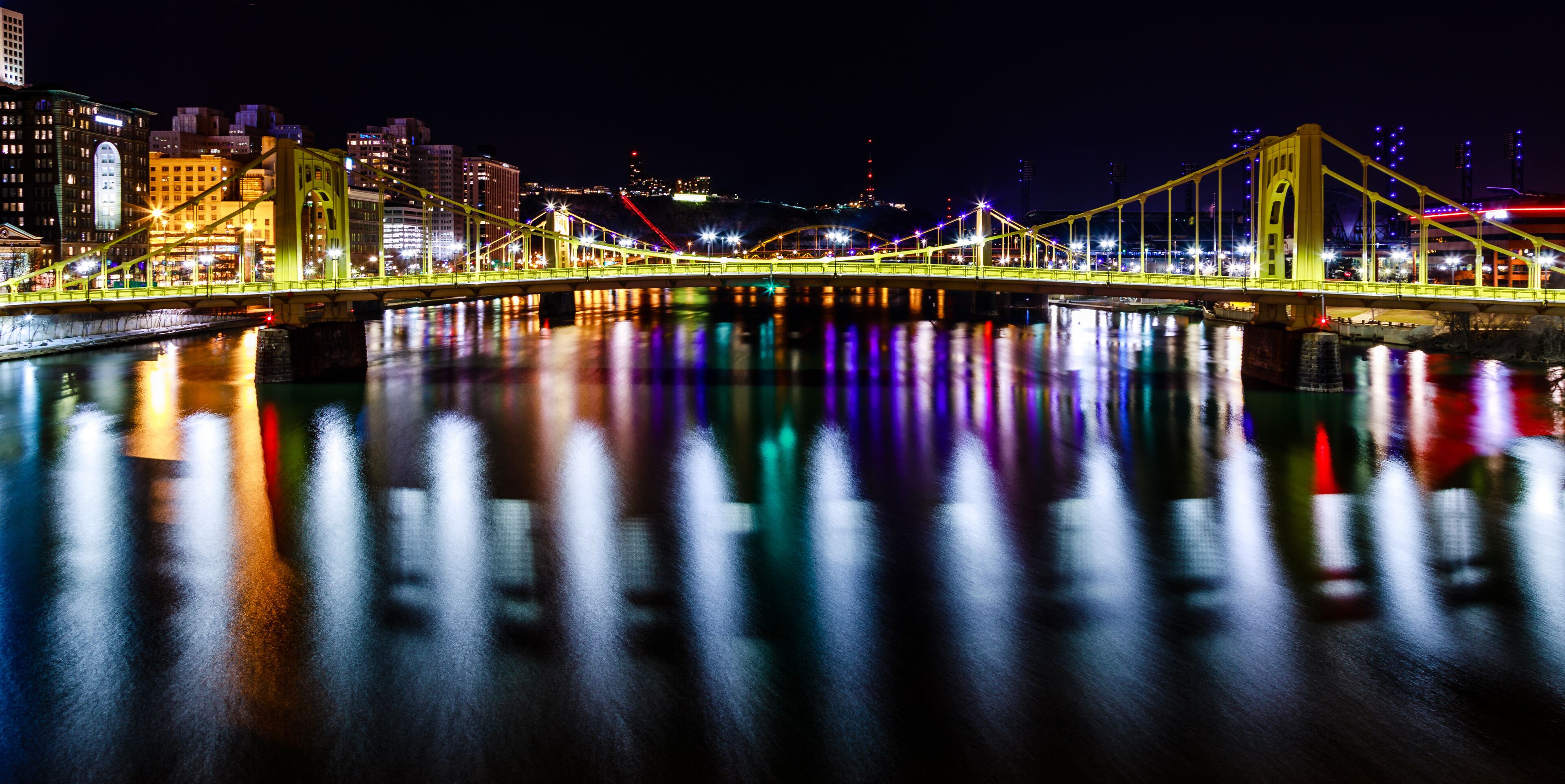A brightly lit bridge with reflections on the water at night.