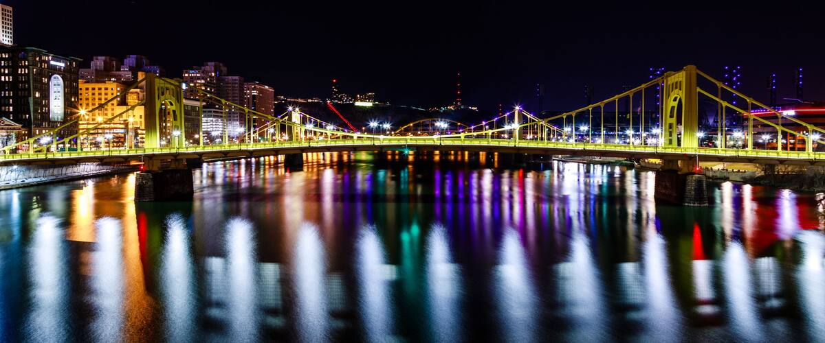 A brightly lit bridge with reflections on the water at night.