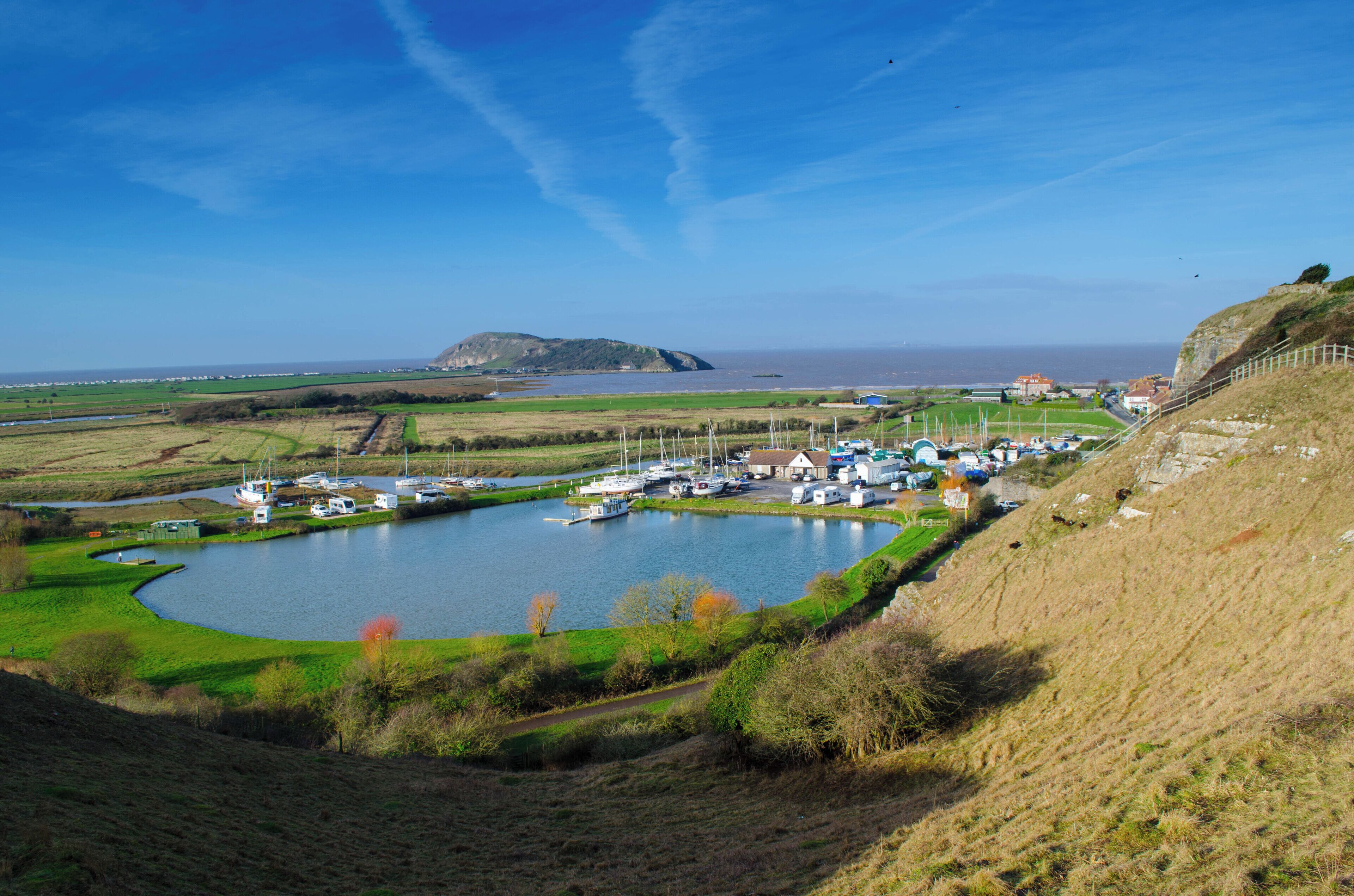 A coastal marina with boats, a small hill, and a distant island.