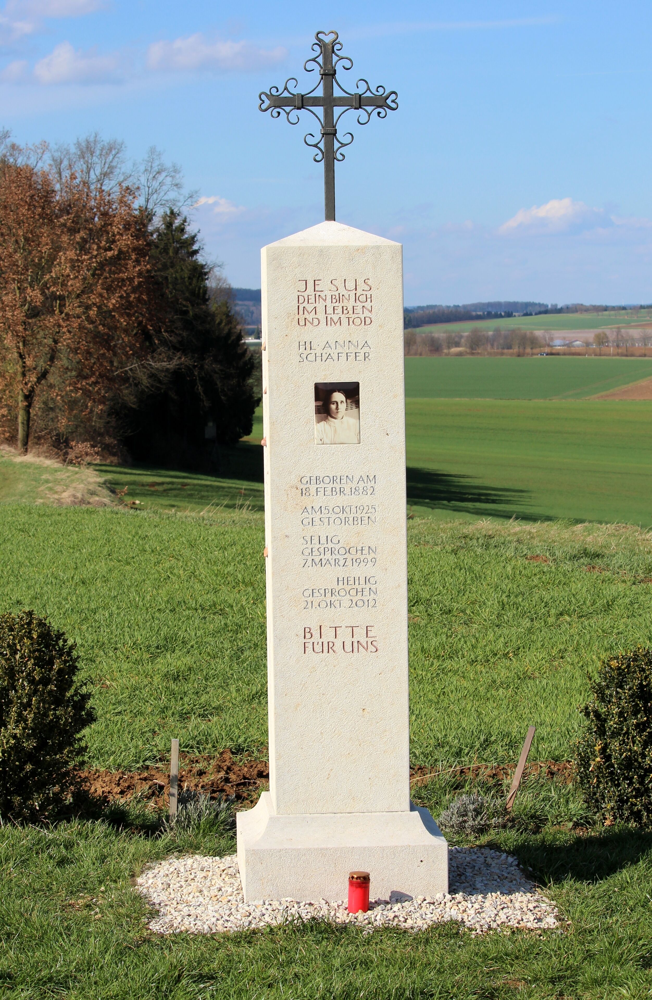 A memorial cross with inscriptions and a photo, surrounded by grass and trees.