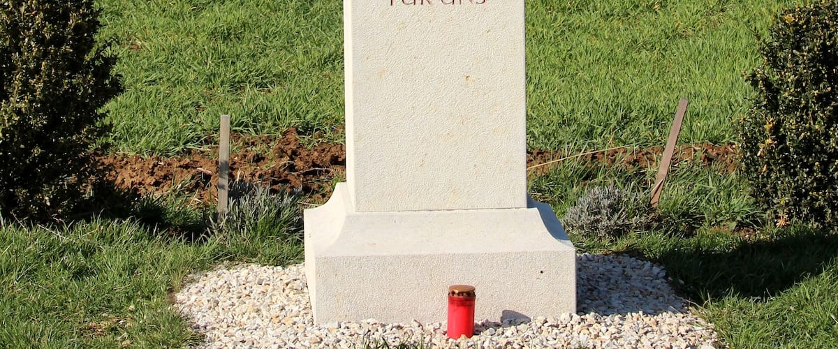 A memorial cross with inscriptions and a photo, surrounded by grass and trees.