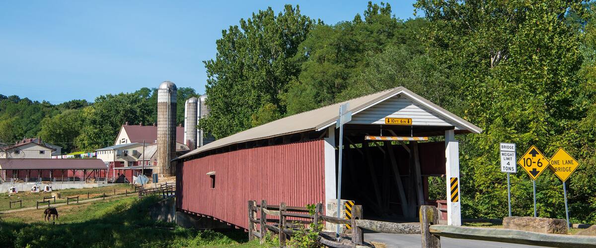 A covered bridge, farm buildings, and silo structures in a rural setting.