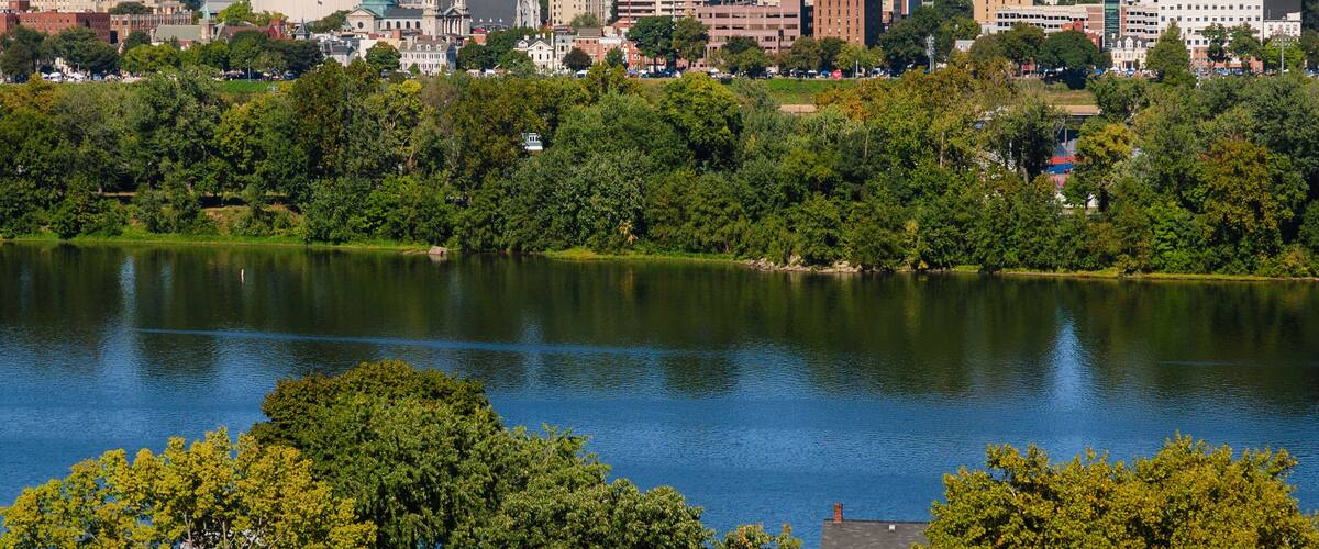 A city skyline with a large lake in the foreground and a hill in the background.