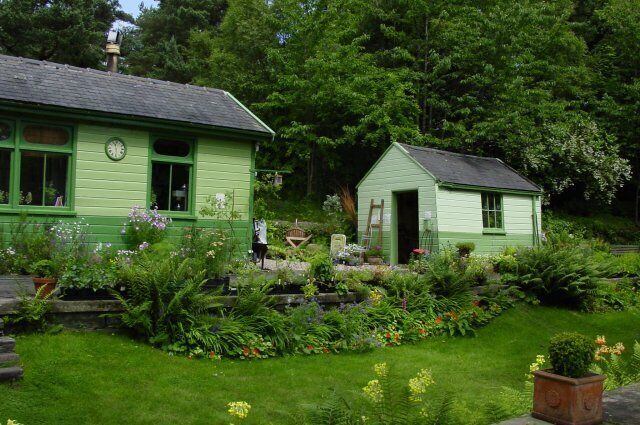 A green house with a clock, surrounded by a garden with various plants and flowers.
