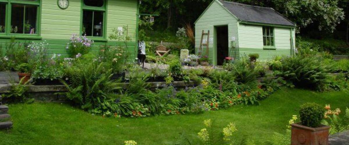 A green house with a clock, surrounded by a garden with various plants and flowers.