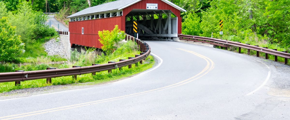 A red covered bridge with a sign reading "Clearance 8' 2\" on a winding road surrounded by lush greenery.