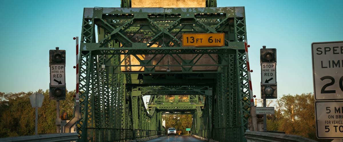 A green metal bridge with a height limit sign of 13 ft 6 in.