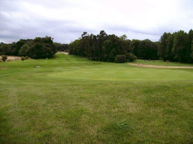 A golf course with a putting green, sand bunkers, and trees in the background.