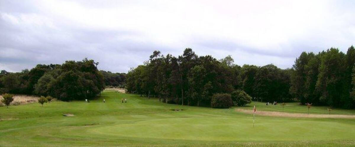 A golf course with a putting green, sand bunkers, and trees in the background.