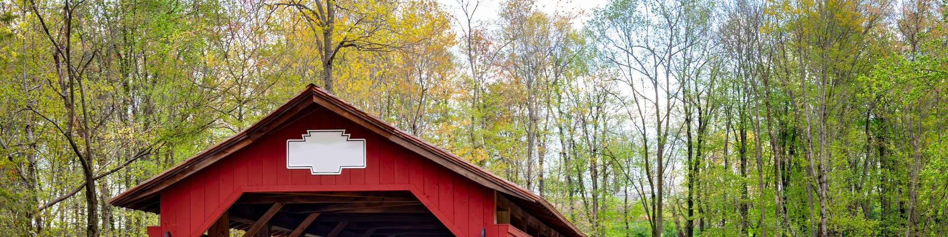A red covered bridge with stone walls, surrounded by trees and blooming flowers.
