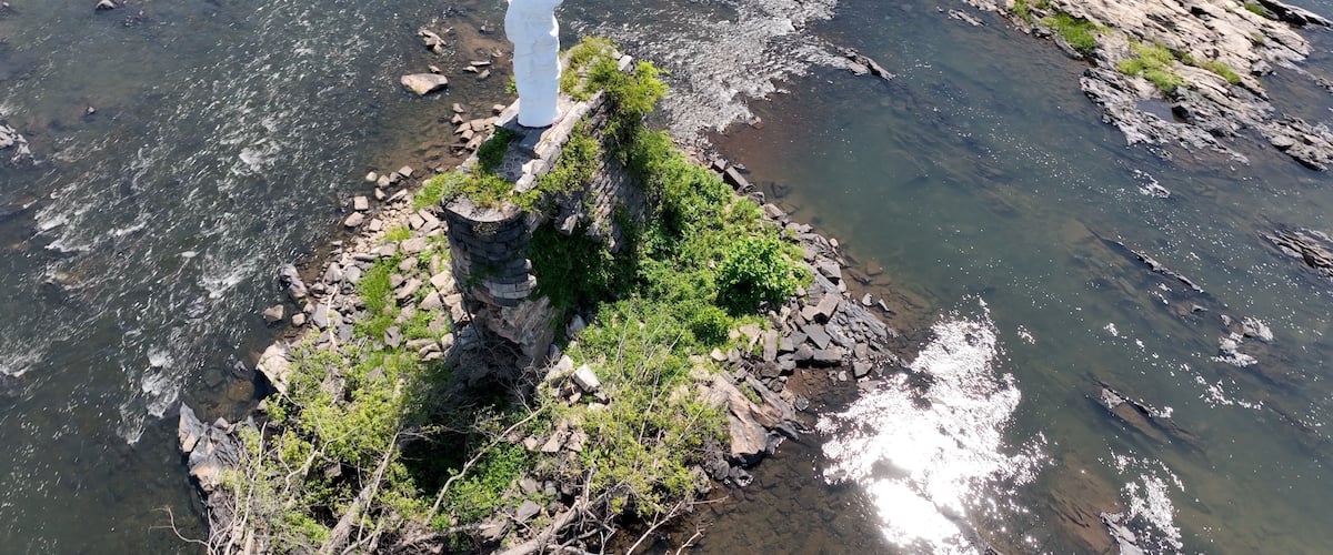 A rocky outcrop with a statue of a figure, surrounded by clear water and greenery.