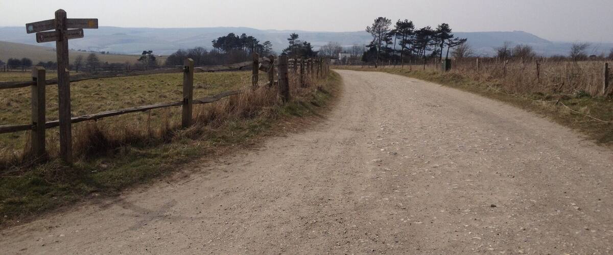 A gravel road with a wooden fence and a directional signpost.