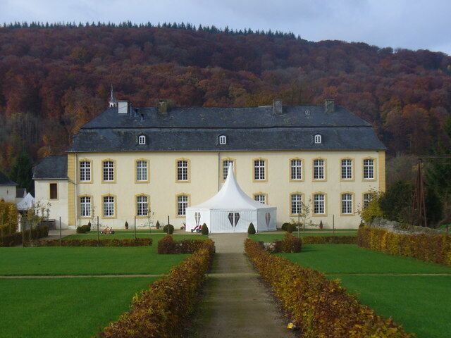A large yellow building with a white tent in front, surrounded by green lawns and autumn-colored trees.