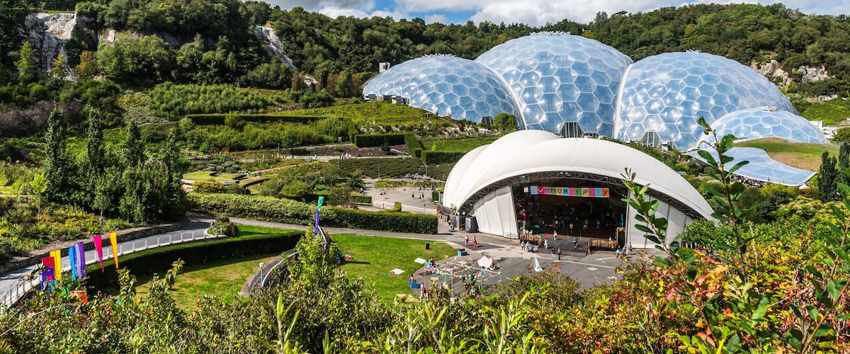 Un edifici gran de forma daurada i color blanc amb un dibuix hexagonal, envoltat de vegetació exuberant i turons.
