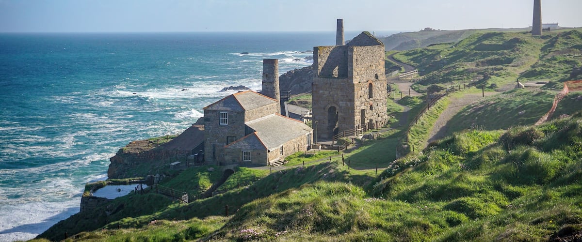 A coastal stone building with a tower, surrounded by grassy hills and the ocean.