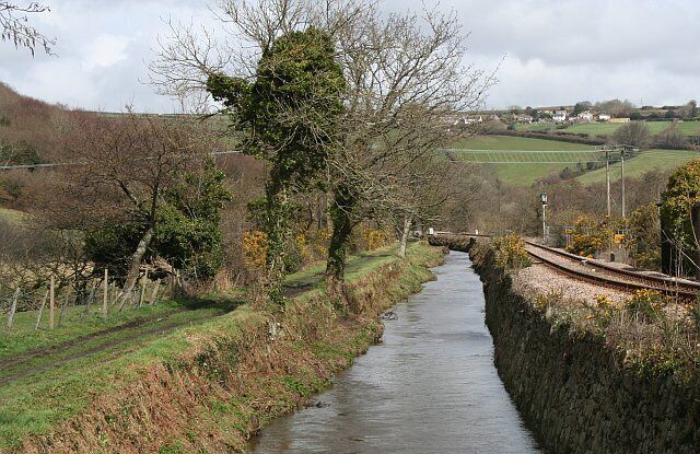 A narrow waterway flanked by trees and a railway track.