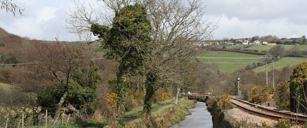 A narrow waterway flanked by trees and a railway track.