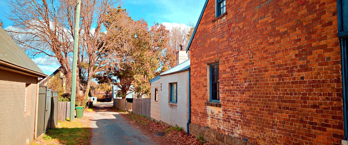 A narrow brick alley with a red brick building on the right and a metal fence on the left.
