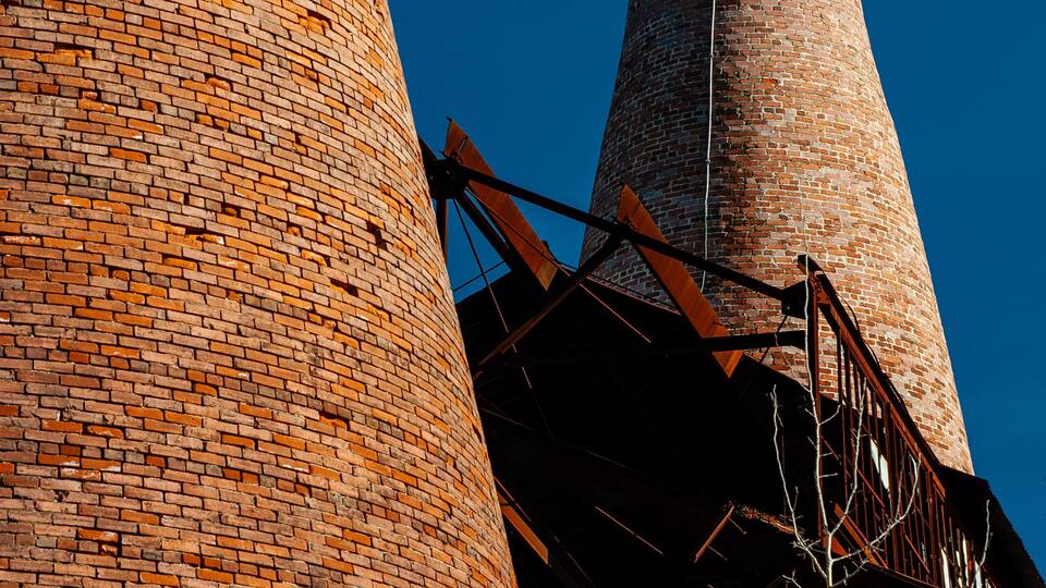 A tall brick chimney with a white-painted base and a metal staircase leading up to a platform.