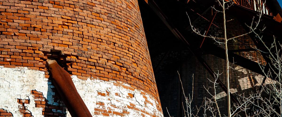 A tall brick chimney with a white-painted base and a metal staircase leading up to a platform.
