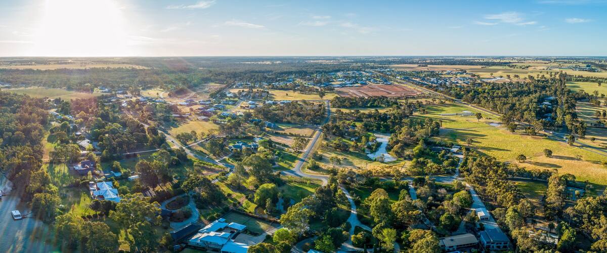 An aerial view of a river winding through a densely forested area with scattered residential buildings and open fields.