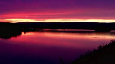 A sunset over a calm lake with a dark silhouette of a forest in the background.