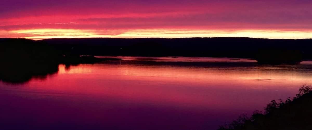 A sunset over a calm lake with a dark silhouette of a forest in the background.