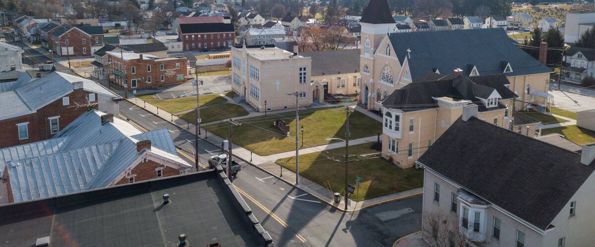 A town with a prominent church featuring a tall steeple and a large cross, surrounded by residential buildings and a clear sky.
