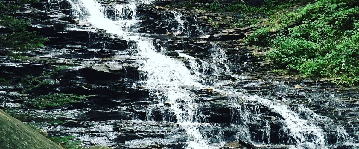 A multi-tiered waterfall surrounded by dense forest.