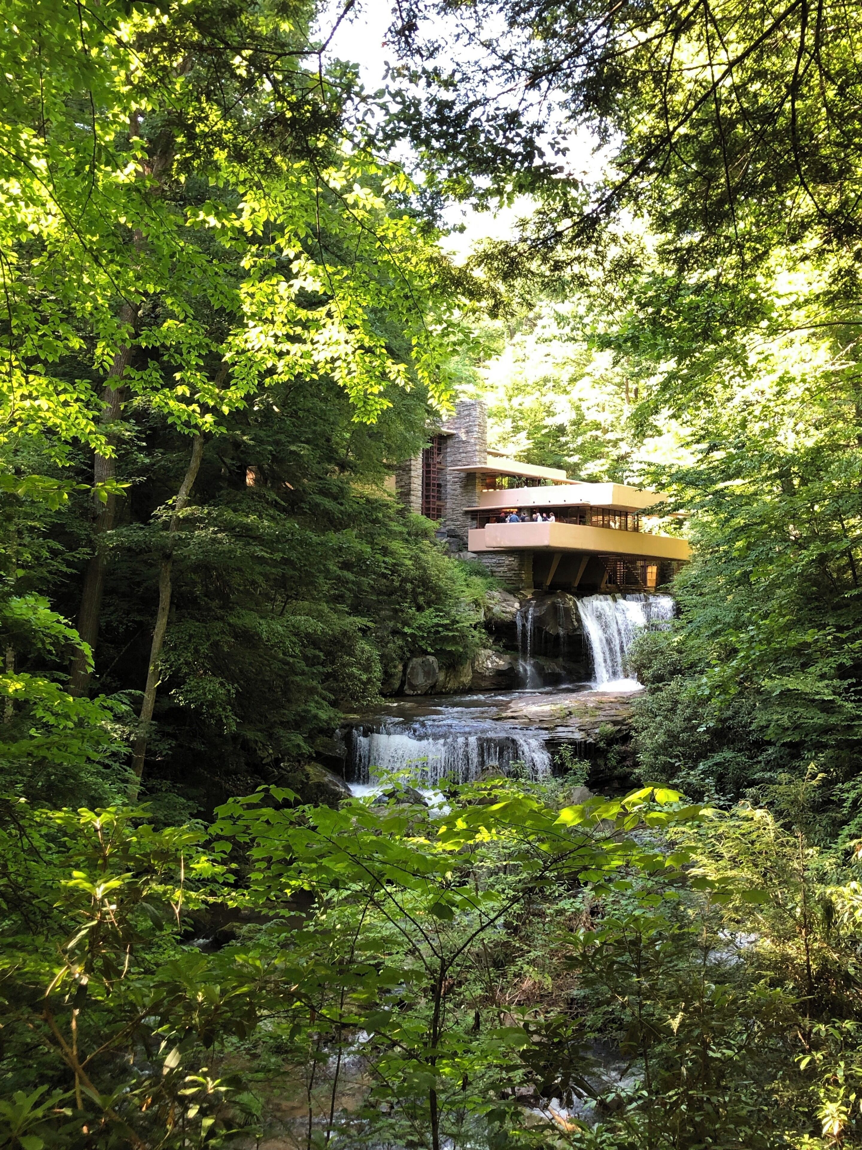 A waterfall cascading into a forested area with a modern building in the background.