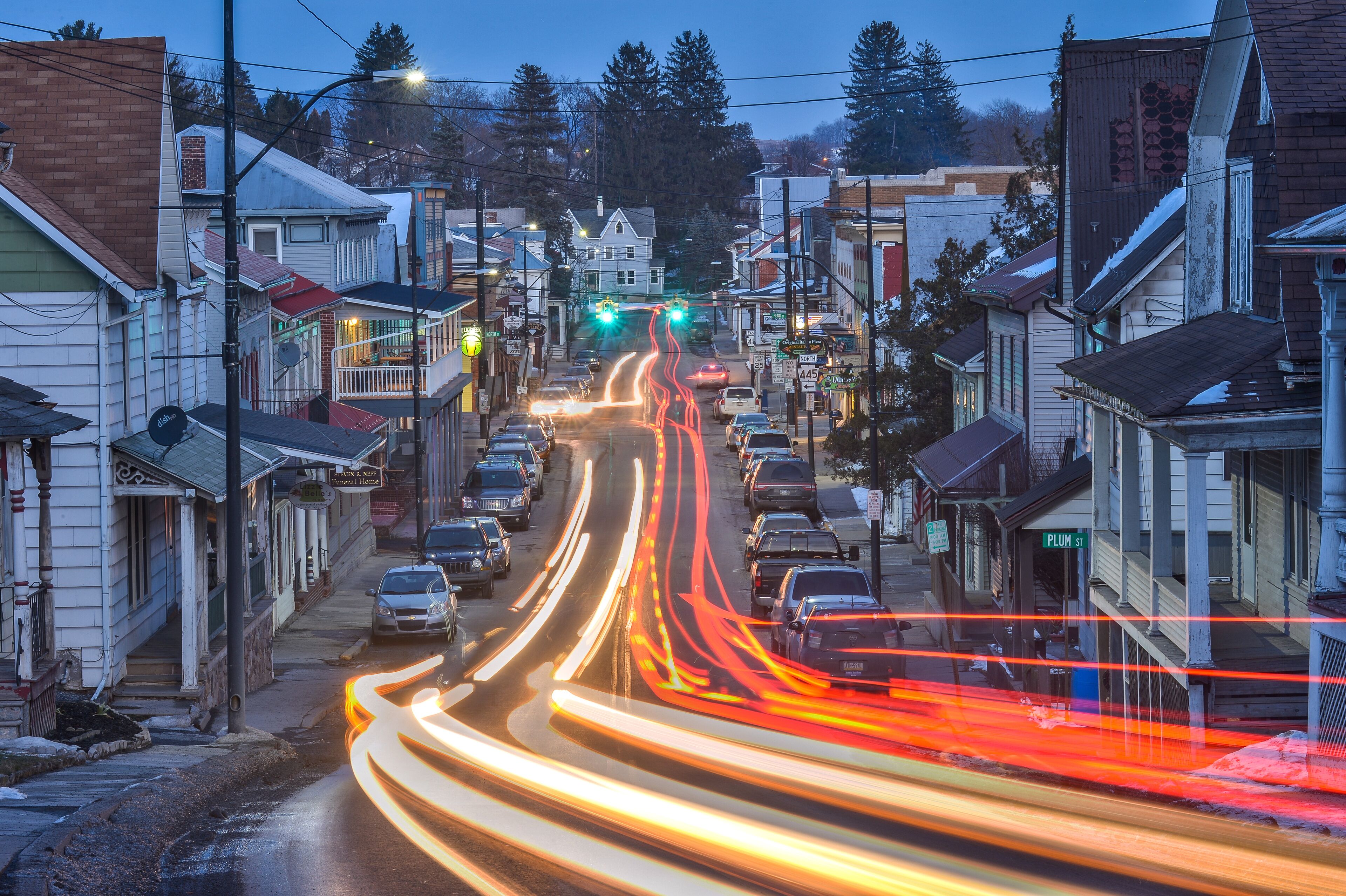 A street with cars and light trails, surrounded by buildings and trees.