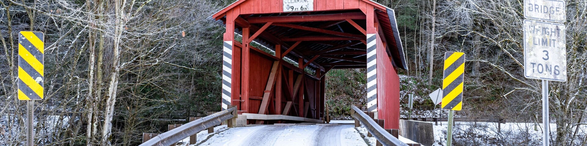 Uma estrada coberta de neve que leva a uma ponte vermelha com um aviso indicando um limite de peso de 3 toneladas.