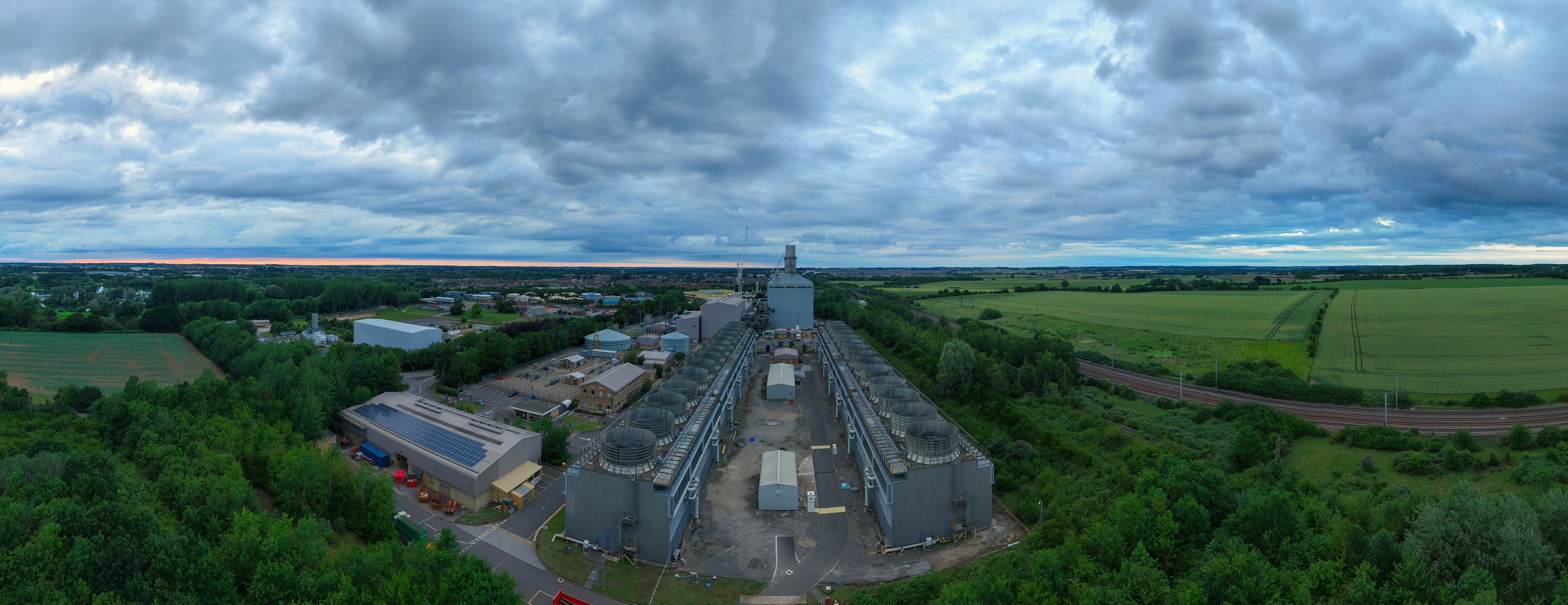 Aerial view of Little Barford Power Station with its industrial buildings, cooling towers, and surrounding green fields under a cloudy sky in St. Neots, England, United Kingdom.