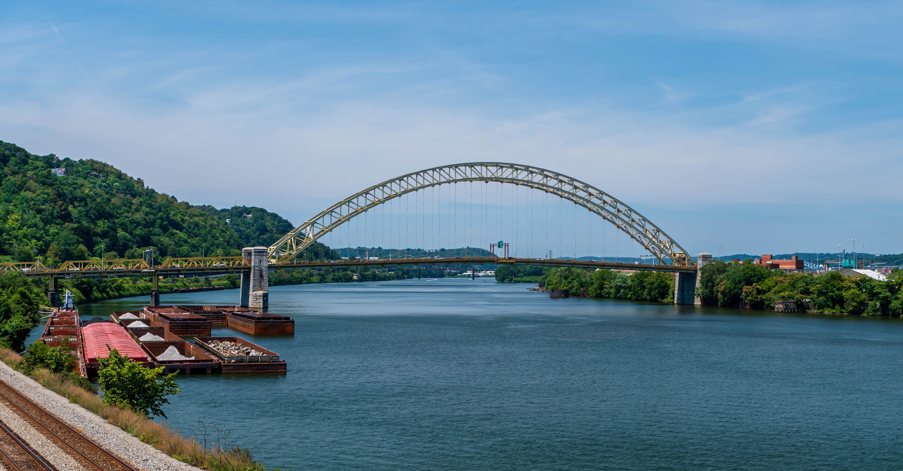 The West End Bridge that spans the Ohio River and connects the north side and the west end in Pittsburgh, Pennsylvania, USA. Several barges and a tugboat are moored to the west end shoreline