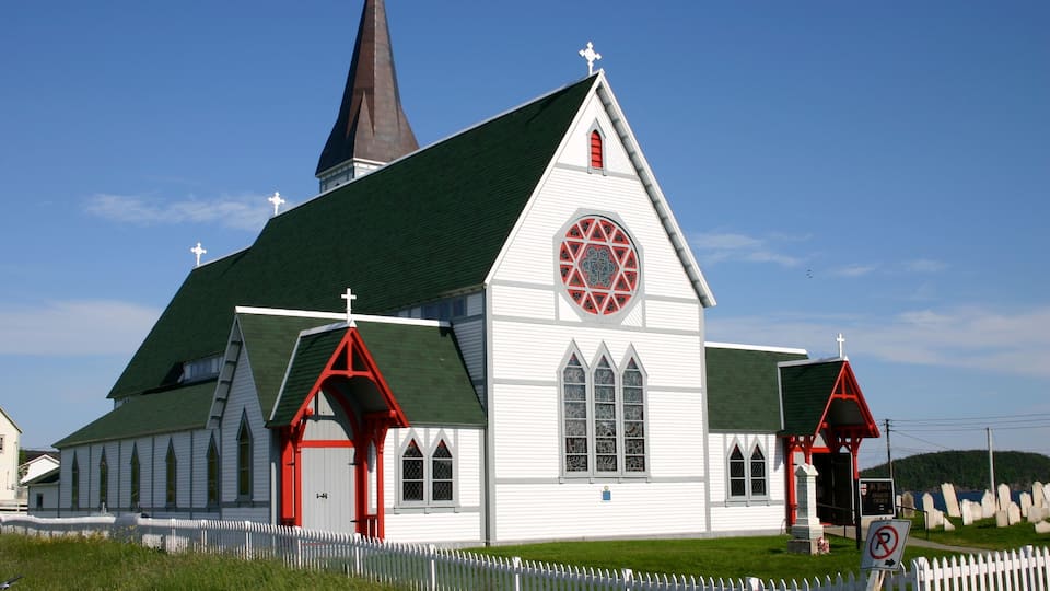 A white church with a green roof and red accents, surrounded by a white picket fence.