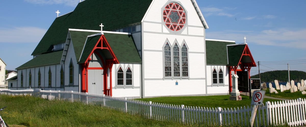 A white church with a green roof and red accents, surrounded by a white picket fence.