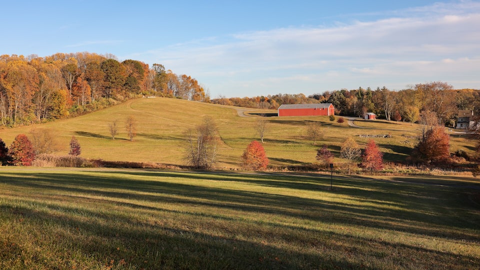 A rural landscape with a red barn, rolling hills, and autumn-colored trees.