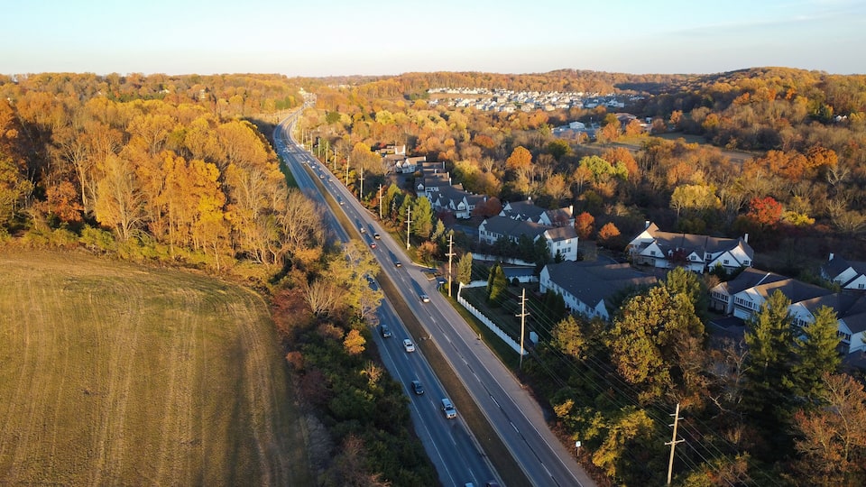 An aerial view of a suburban area with a highway, houses, and autumn-colored trees.