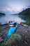 Un kayak azul sobre una orilla rocosa, con un lago tranquilo y colinas boscosas al fondo.