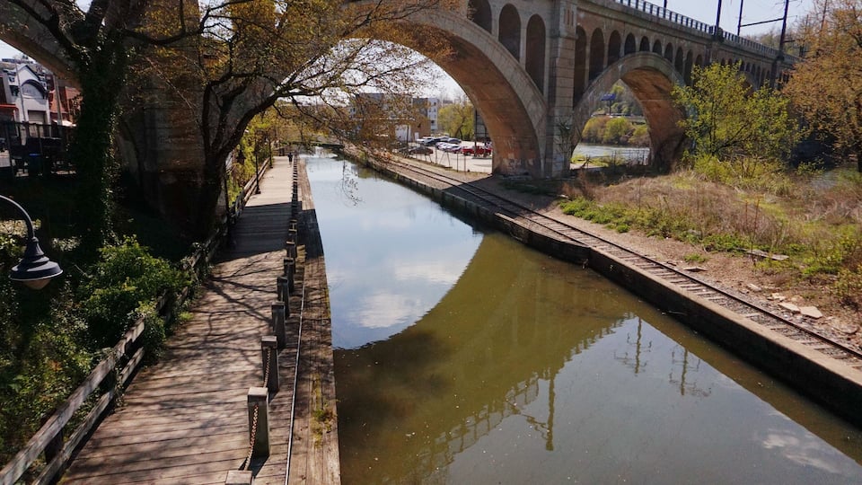 A river with a wooden walkway and a stone bridge in the background.