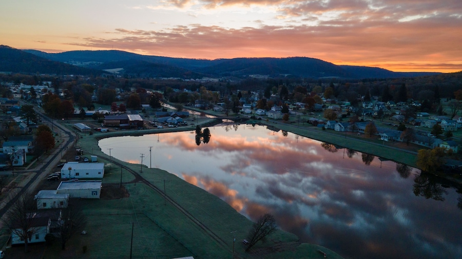 Un atardecer sobre un pequeño pueblo con un estanque central que refleja el cielo.