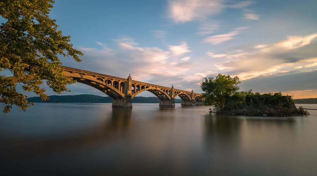 A bridge over calm water with trees on the left and a small island on the right.