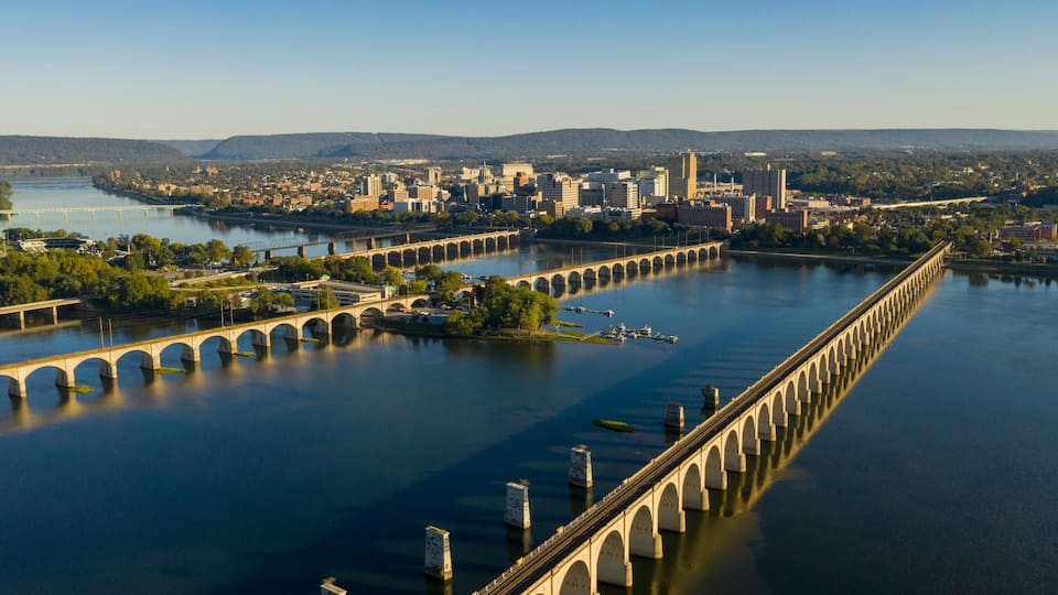 A river with a long bridge spanning across it, surrounded by a cityscape with buildings and hills in the background.