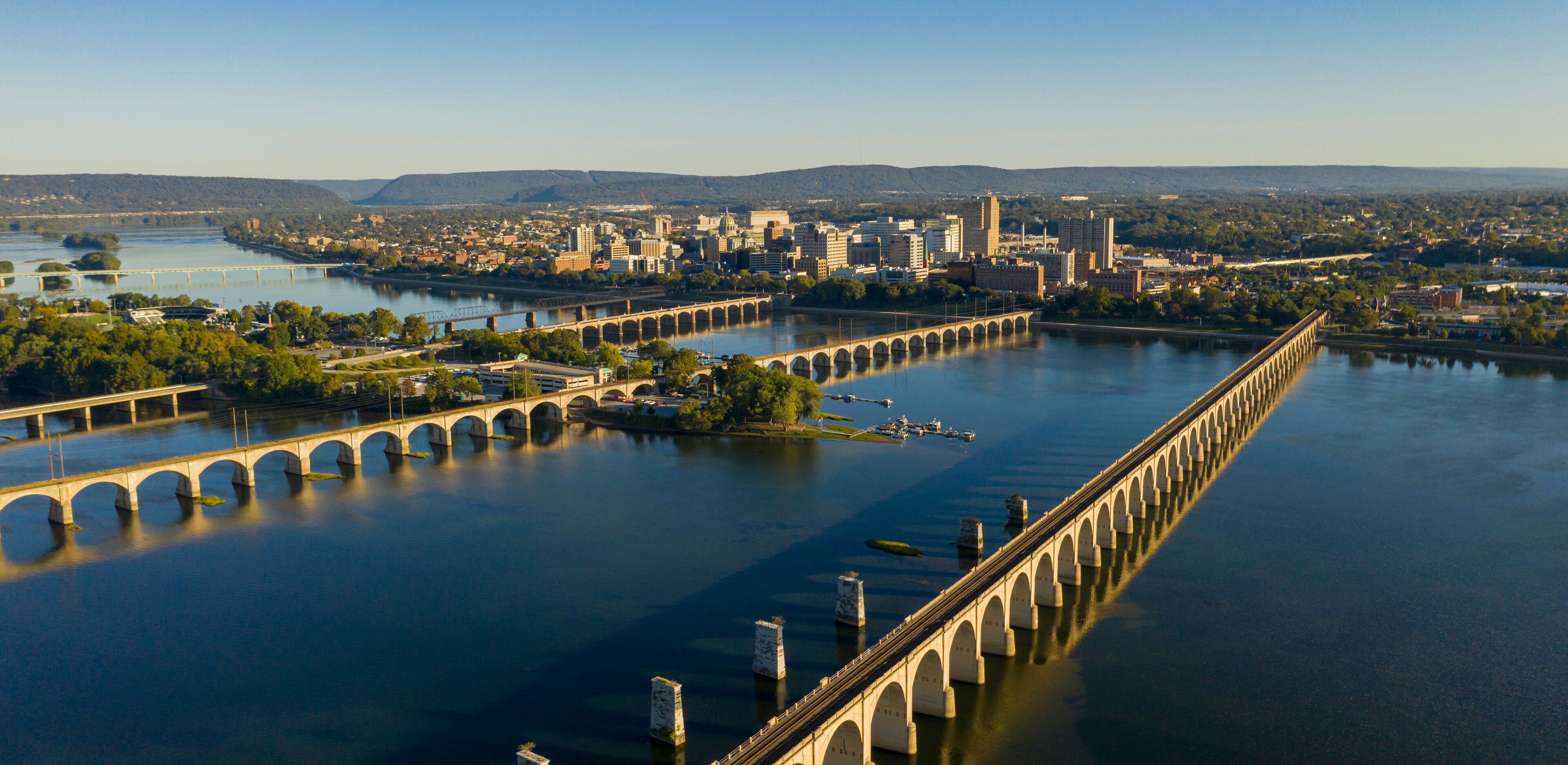 A river with a long bridge spanning across it, surrounded by a cityscape with buildings and hills in the background.