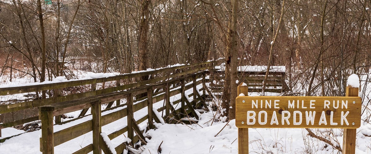 A wooden sign engraved with Nine Mile Run Boardwalk, a stream and walkway in Frick Park, an urban park in Pittsburgh, Pennsylvania, USA as seen on a sunny winter day