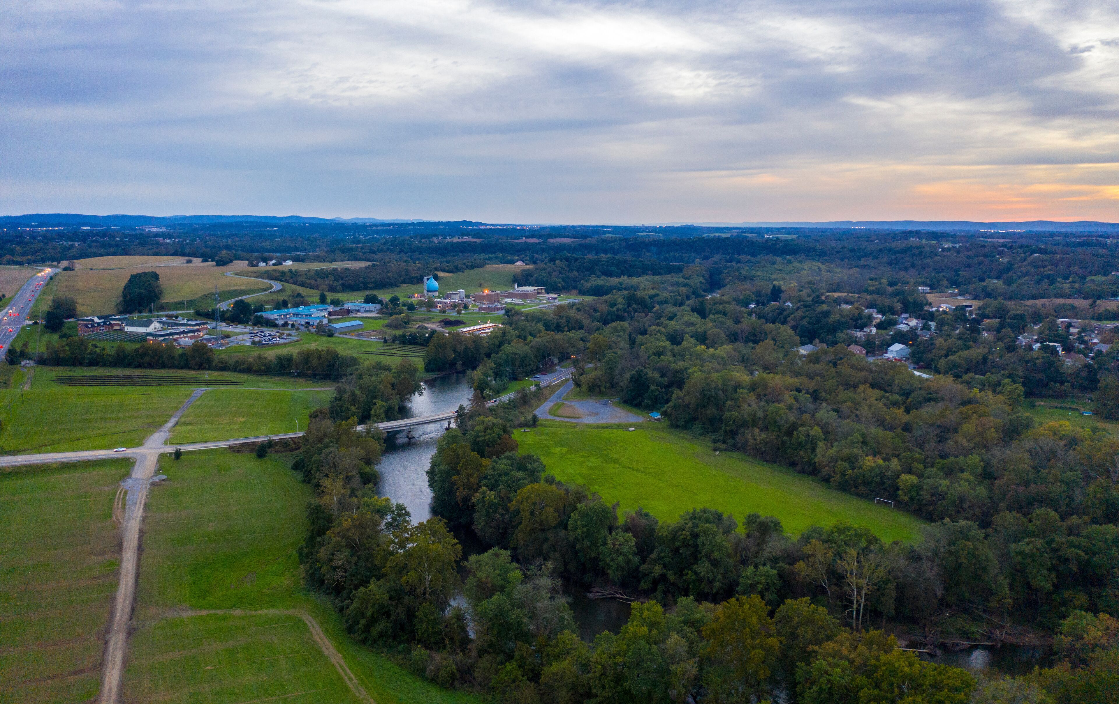 An aerial view of a town with a river, green fields, and industrial buildings.