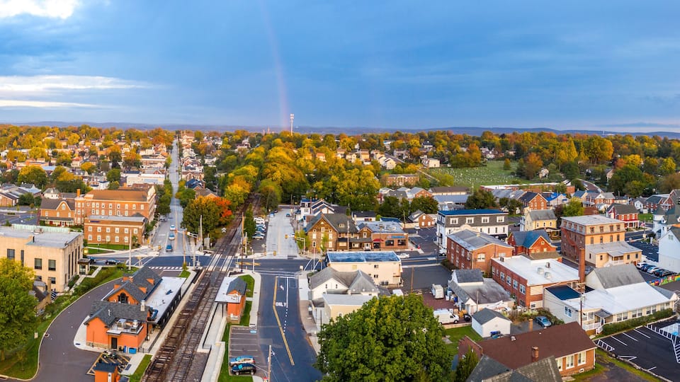 A town with a railroad track, buildings, and autumn-colored trees.