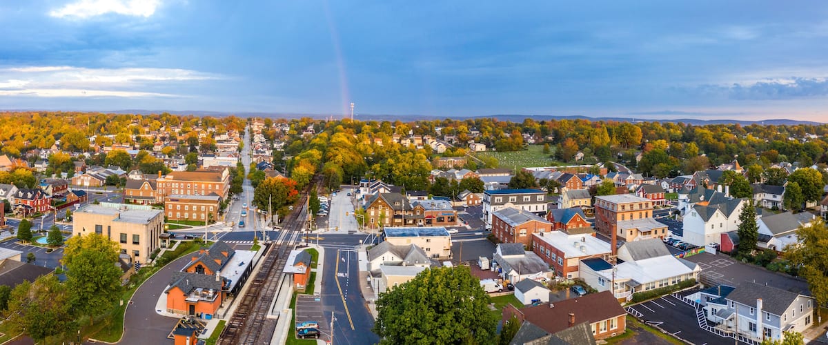 A town with a railroad track, buildings, and autumn-colored trees.