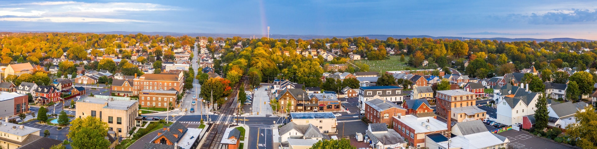 A town with a railroad track, buildings, and autumn-colored trees.